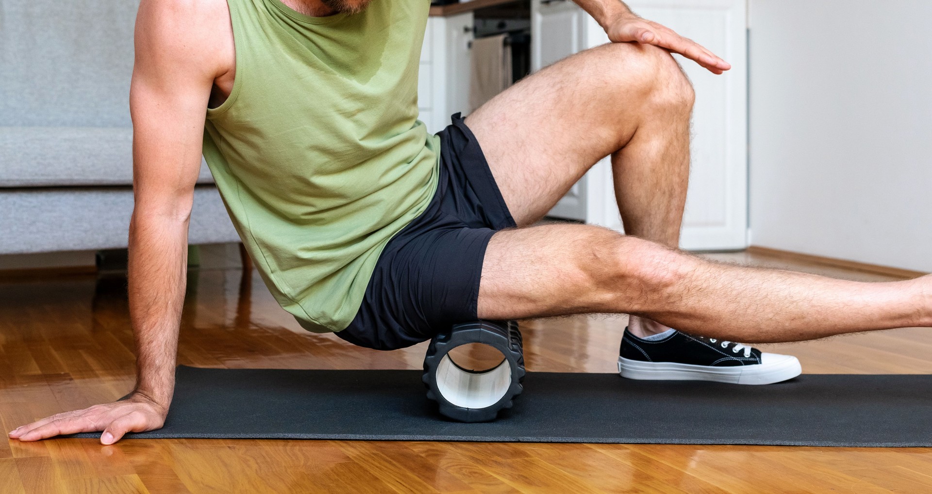 Male athlete doing fitness exercise using foam roller, home workout.