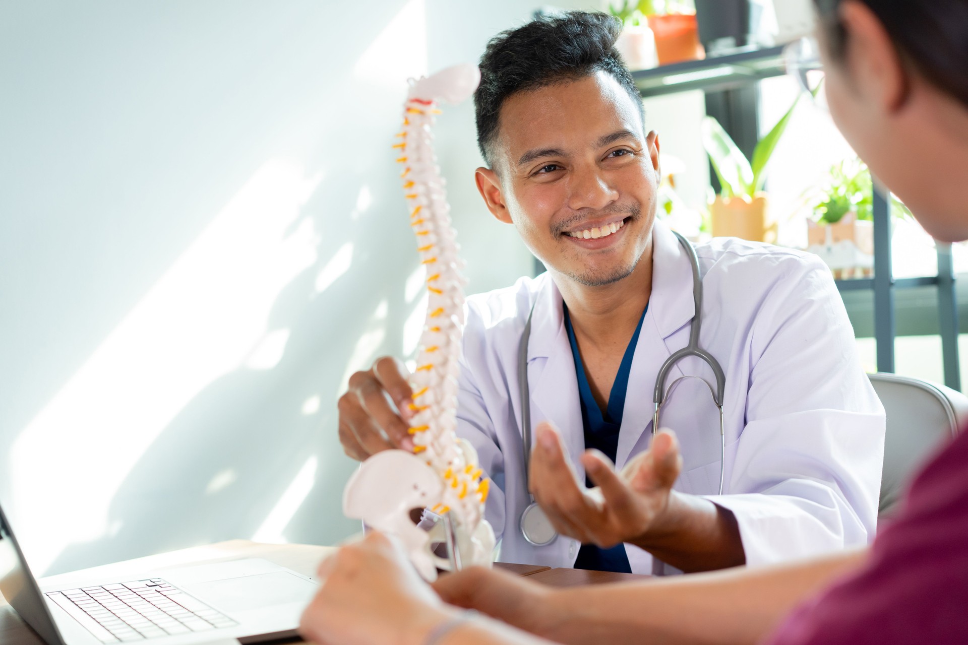 close up physical therapist explain on human skeleton at low back to advise and consult to patient to treatment at office for healthcare concept